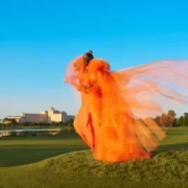 Model standing on the golf course in an orange dress in front of Rosen