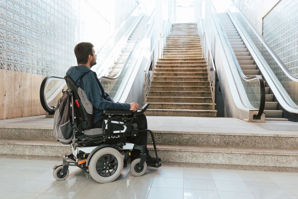 Man in wheelchair looking at small set of stairs that lead to an escalator