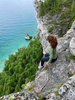 Photo of Aracelly Delgadillo sitting on a cliff, with blue water far down below.