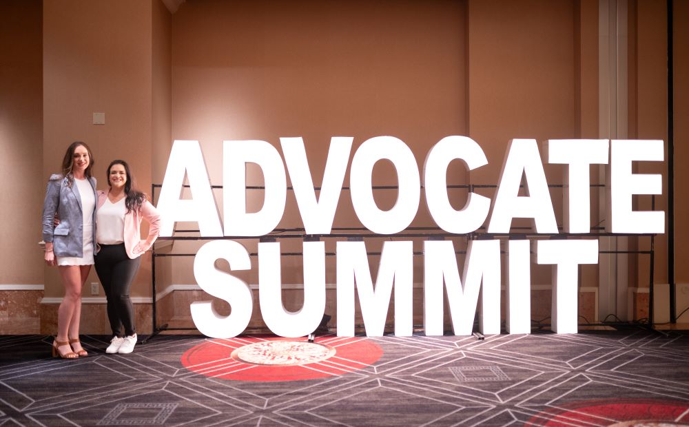 Photo of two attendees standing next to Healthcare Advocate Summit signage.