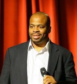 Photo of speaker Andre Norman with a mic in front of a red curtain.