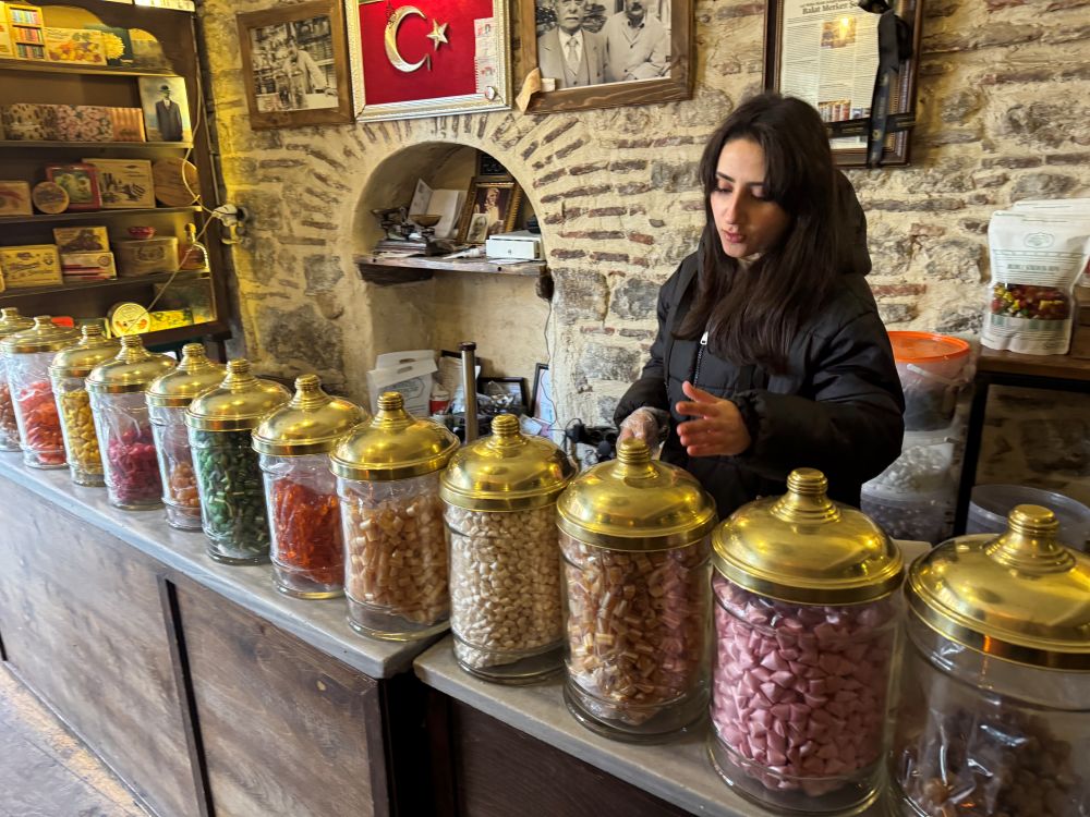 Photo of a woman standing in front of many candy jars at Balat Merkez Confectionery.