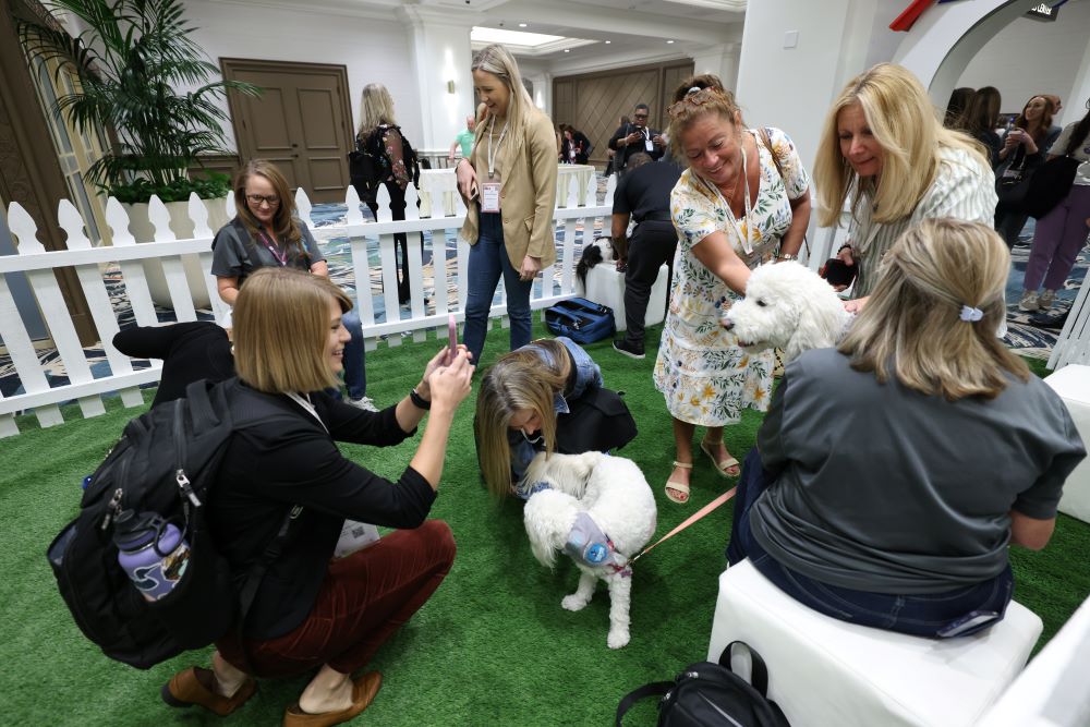 Photo of Danielle LeBreck taking a photo at the puppy cuddling booth at IMEX America 2023.