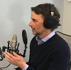 Photo of David Coriale in headphones, podcasting.