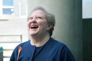 Photo of Joan Eisenstodt looking up and laughing, in a blue dress.