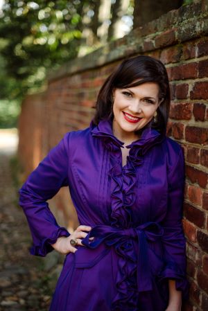 Photo of KiKi L'Italien standing in a purple dress in front of a brick wall.