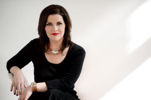 Photo of KiKi L'Italien, sitting in a chair in a black dress.