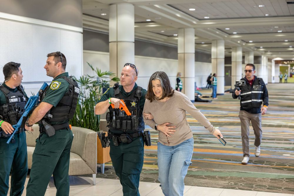 Photo of actor pretending to be injured, next to a police officer with a mock orange gun.