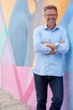 Photo of Philip Dunlap standing in front of a colorful wall in a blue shirt.