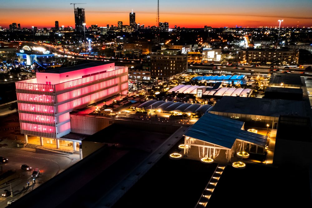 Photo of POST Houston, glowing pink in front of Houston skyline.