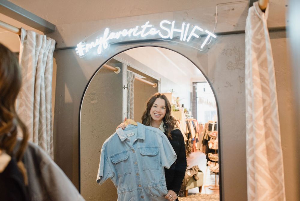 Photo of Shift Boutique, with woman looking in mirror holding a shirt.