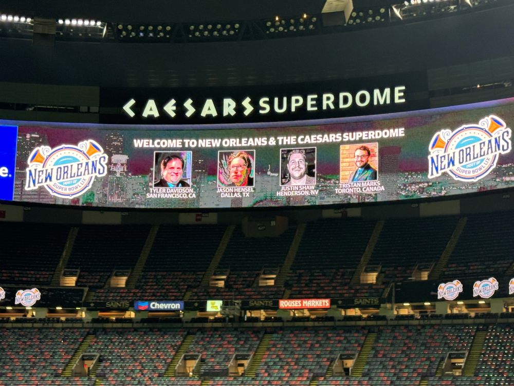 Video screen in Caesars Superdome showing writers who attended Super Bowl fam.