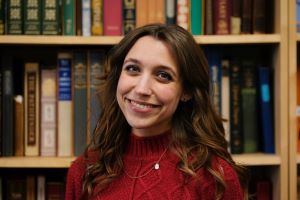 Photo of Taylor Smith in red sweater, in front of book stacks.