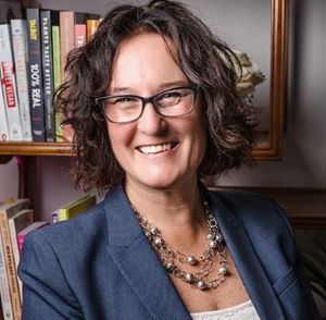 Photo of Tracy Stuckrath, smiling in a blue blazer in front of a book shelf.