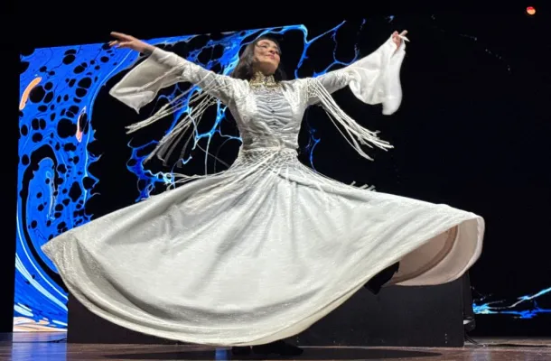 Photo of a Sufi dancer in a flowing white dress twirling on stage.