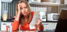 Photo of woman sitting at a desk with her hand on her head, exasperated looking at paperwork.