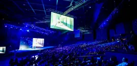 Photo of a group gathered in a large, dark convention hall to see a keynote presentation.