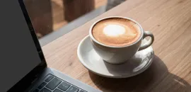 Cup of coffee on a table next to a laptop