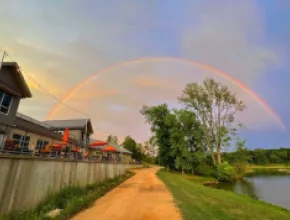 A dirt road along a body of water with a rainbow in the sky.