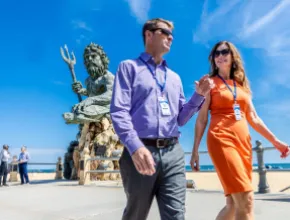 Man and woman attendees walking with King Neptune statue in the background in Virginia Beach