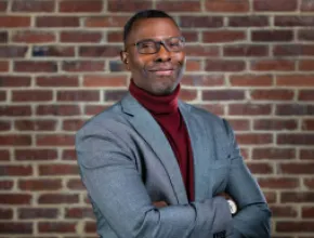 Photo of Elliott L. Ferguson II standing in front of a brick wall in a gray blazer.