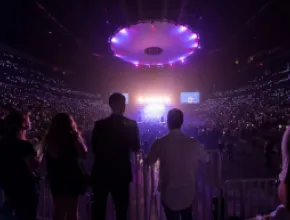 Photo of people looking at a concert, in a venue filled with purple light.