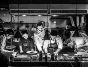 Black-and-white photo of a chef and assistants working in a kitchen.