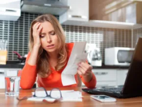 Photo of woman sitting at a desk with her hand on her head, exasperated looking at paperwork.