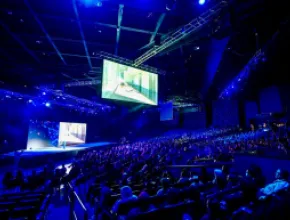 Photo of a group gathered in a large, dark convention hall to see a keynote presentation.