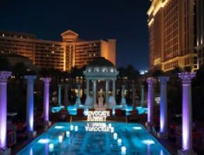 Photo of Caesars Palace pool with Advocate Summit sign lit up, at night.