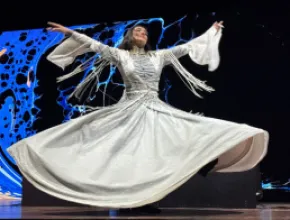 Photo of a Sufi dancer in a flowing white dress twirling on stage.