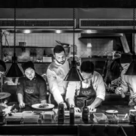 Black-and-white photo of a chef and assistants working in a kitchen.