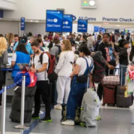 Photo of frustrated travelers standing in line at an airline check-in counter.