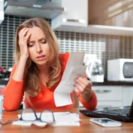 Photo of woman sitting at a desk with her hand on her head, exasperated looking at paperwork.