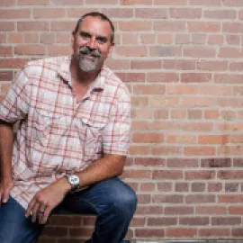 Photo of Mike McCallen standing in front of a brick wall.