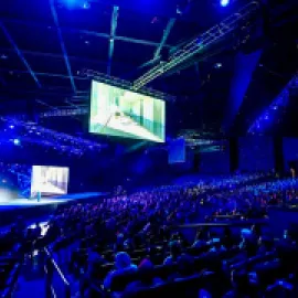 Photo of a group gathered in a large, dark convention hall to see a keynote presentation.