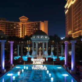 Photo of Caesars Palace pool with Advocate Summit sign lit up, at night.