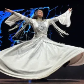 Photo of a Sufi dancer in a flowing white dress twirling on stage.