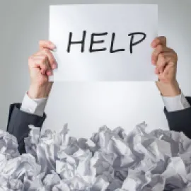 Image of a person holding a paper with the word HELP written on it, emerging from a bunch of crumpled up papers.