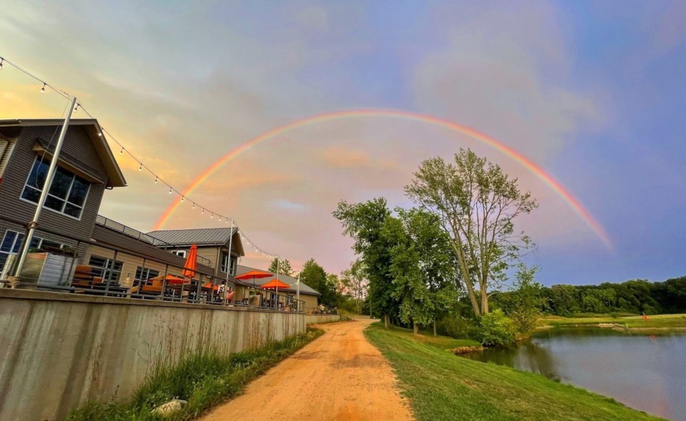 A dirt road along a body of water with a rainbow in the sky.