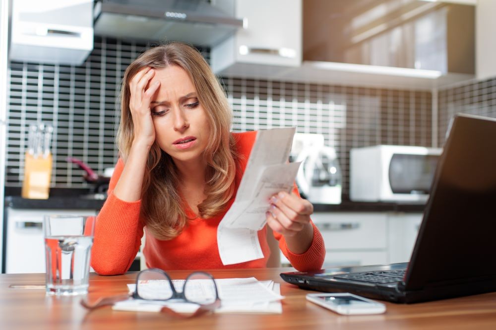 Photo of woman sitting at a desk with her hand on her head, exasperated looking at paperwork.