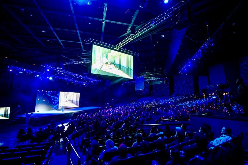 Photo of a group gathered in a large, dark convention hall to see a keynote presentation.