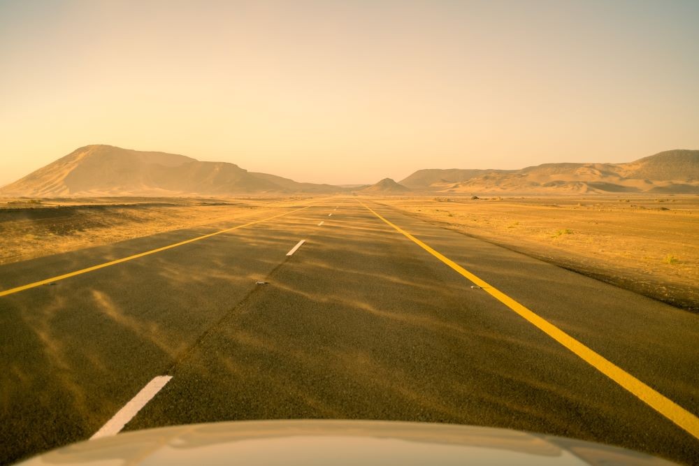 Photo of a road with sand blowing across it.