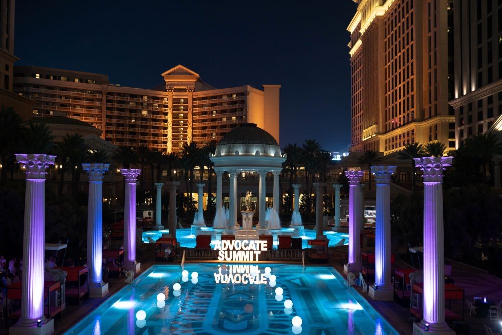 Photo of Caesars Palace pool with Advocate Summit sign lit up, at night.