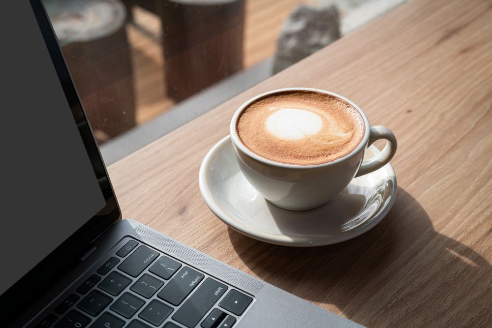 Cup of coffee on a table next to a laptop