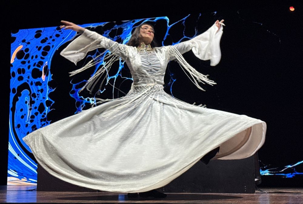 Photo of a Sufi dancer in a flowing white dress twirling on stage.