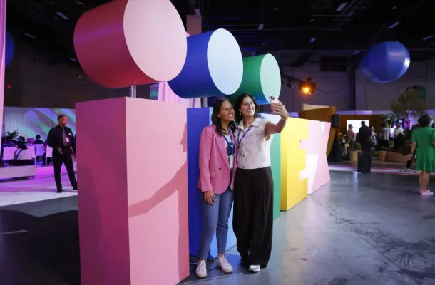 Two attendees take a selfie in front of the IMEX sign